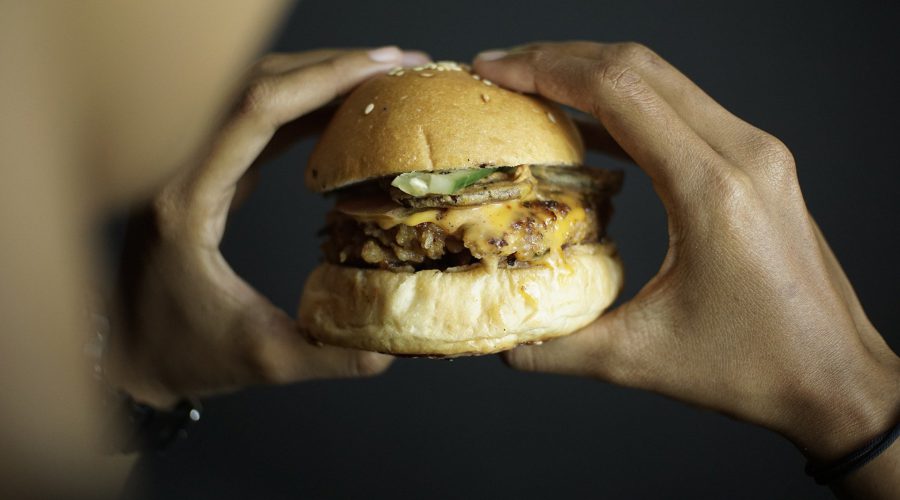 Iemand die een hamburger vasthoudt, ter illustratie bij het nieuwsbericht dat wethouders van de G4 een wetswijziging willen voor een gezondere voedselomgeving