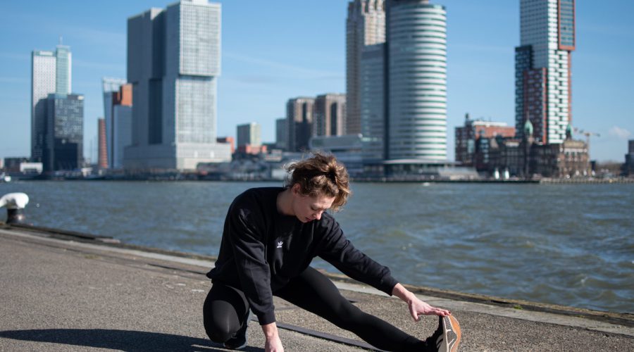 Deelnemer van BioCheck programma strekt haar been, met de gebouwen van de Wilhelminapier op de achtergrond