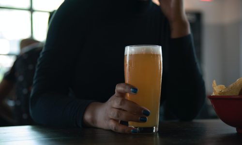 Vrouw in zwart shirt die een vol glas bier vasthoudt