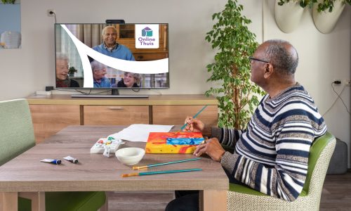 Een oudere man schildert terwijl hij naar Online Thuis op een televisiescherm kijkt