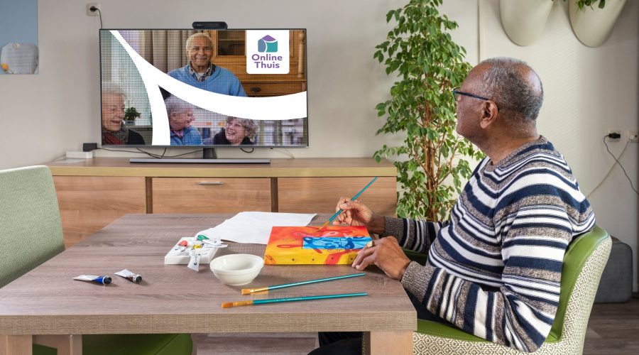 Een oudere man schildert terwijl hij naar Online Thuis op een televisiescherm kijkt