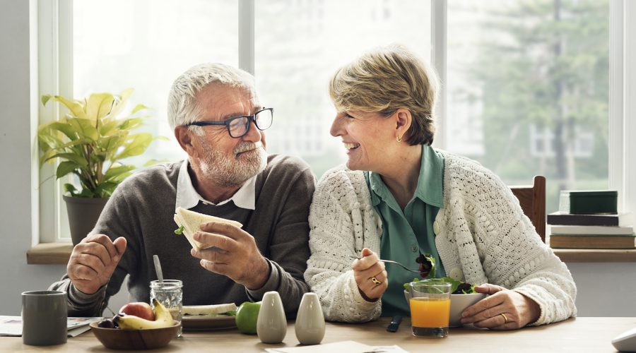 Oudere man en vrouw aan de keukentafel met ontbijt, kijken elkaar blij aan