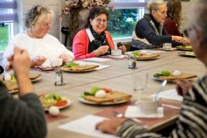 Ouderen aan een grote tafel die met elkaar een gezonde maaltijd eten