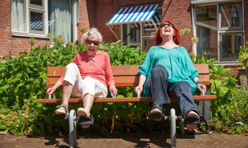 Twee senioren op een bankje in de zon, met een trapwiel om in beweging te blijven