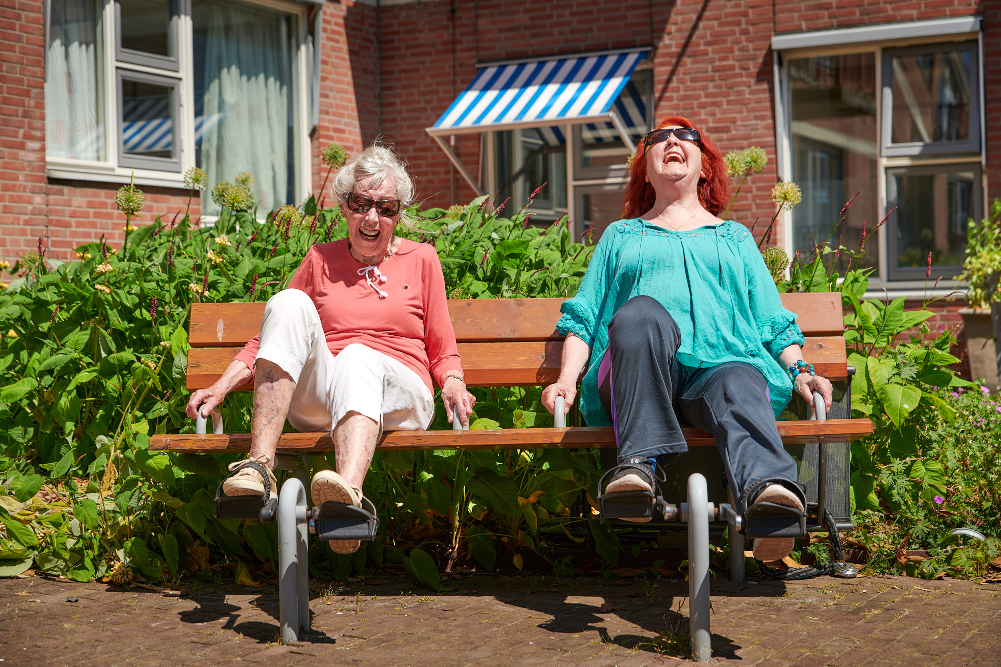 Twee senioren op een bankje in de zon, met een trapwiel om in beweging te blijven